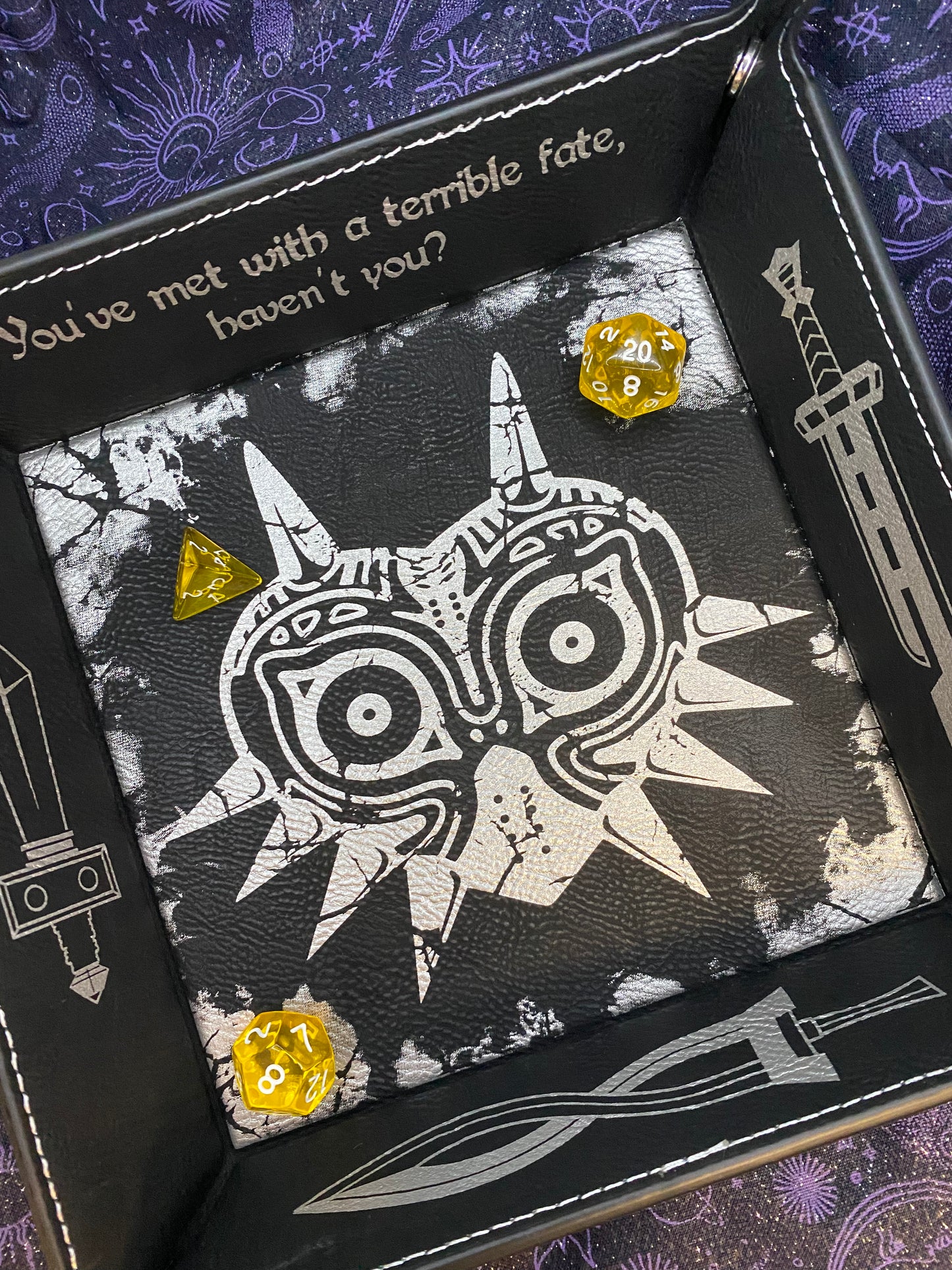 Black leather dice tray featuring a laser engraved Majora’s Mask design and sword icons, inspired by The Legend of Zelda. Ideal for tabletop and D&D fans who love Zelda lore. An alternate version with fog design in corners