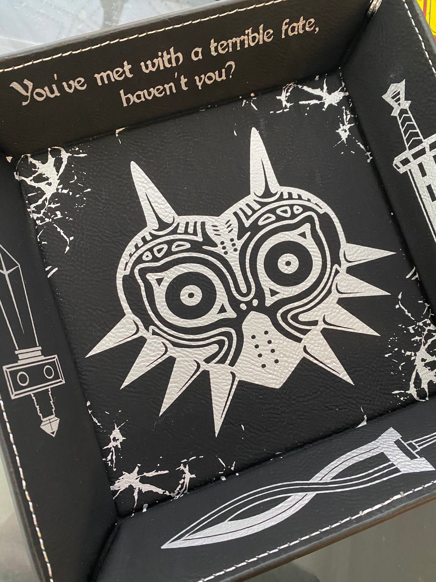 Black leather dice tray featuring a laser engraved Majora’s Mask design and sword icons, inspired by The Legend of Zelda. Ideal for tabletop and D&D fans who love Zelda lore.