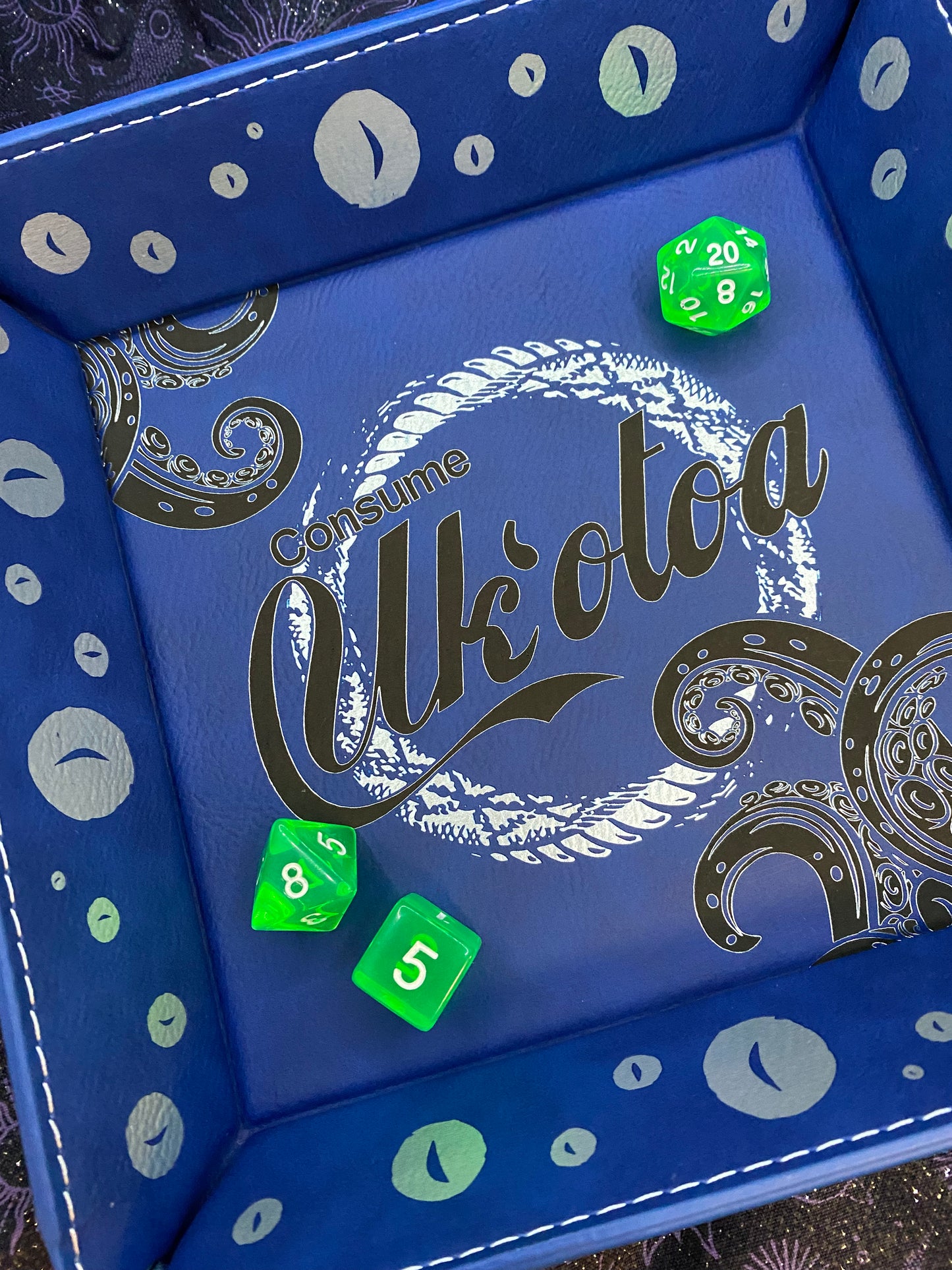 Blue leather dice tray featuring 'Consume Uk'otoa' design with tentacles and sea motifs, inspired by Critical Role's sea monster character, surrounded by green D&D dice