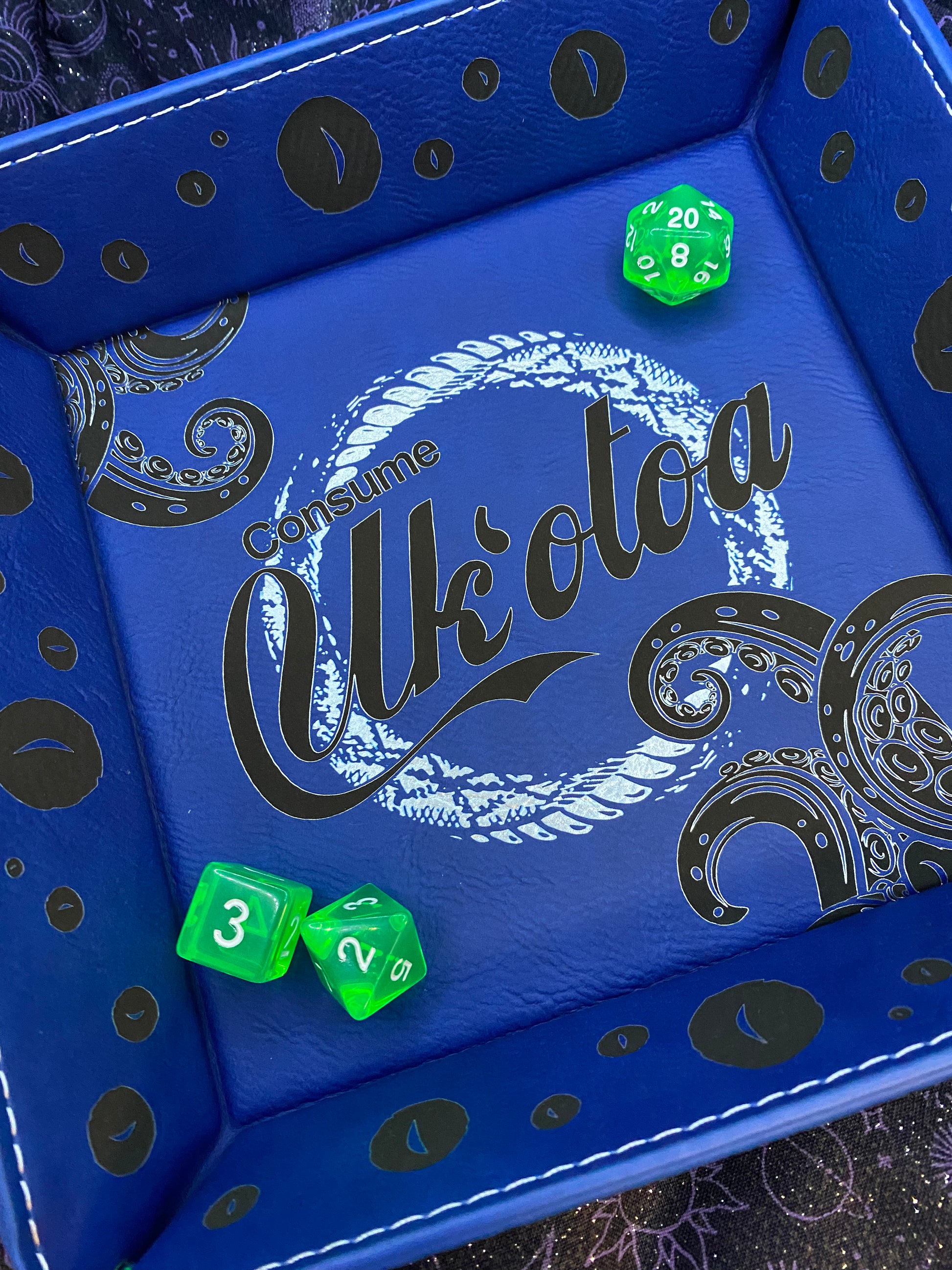 Blue leather dice tray featuring 'Consume Uk'otoa' design with tentacles and sea motifs, inspired by Critical Role's sea monster character, surrounded by green D&D dice, black eyes version